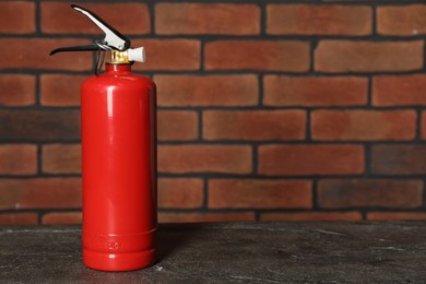 Photo of One red fire extinguisher near brick wall, space for text