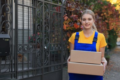 Photo of Courier in uniform with parcels near private house outdoors, space for text