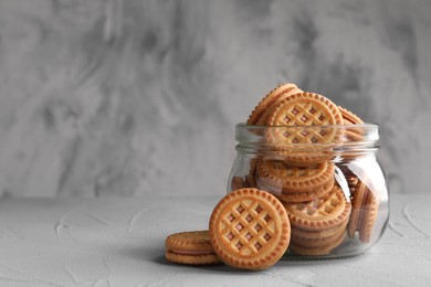 Photo of Tasty sandwich cookies with cream in jar on light grey table, space for text