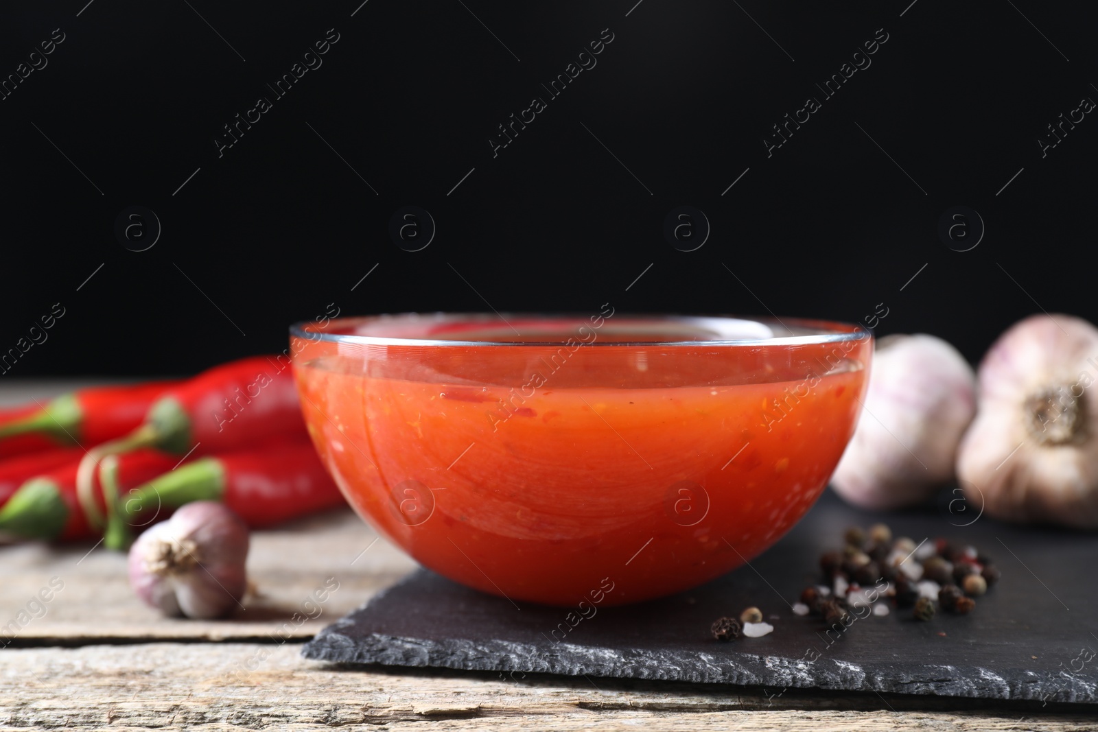 Photo of Spicy chili sauce in bowl on wooden table, closeup