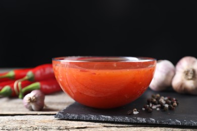 Photo of Spicy chili sauce in bowl on wooden table, closeup