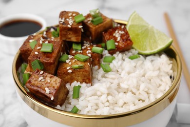 Photo of Bowl of rice with fried tofu and green onions on white marble table, closeup