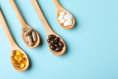 Photo of Wooden spoons with different dietary supplements on light blue background, flat lay. Space for text