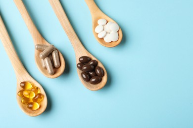 Wooden spoons with different dietary supplements on light blue background, flat lay. Space for text