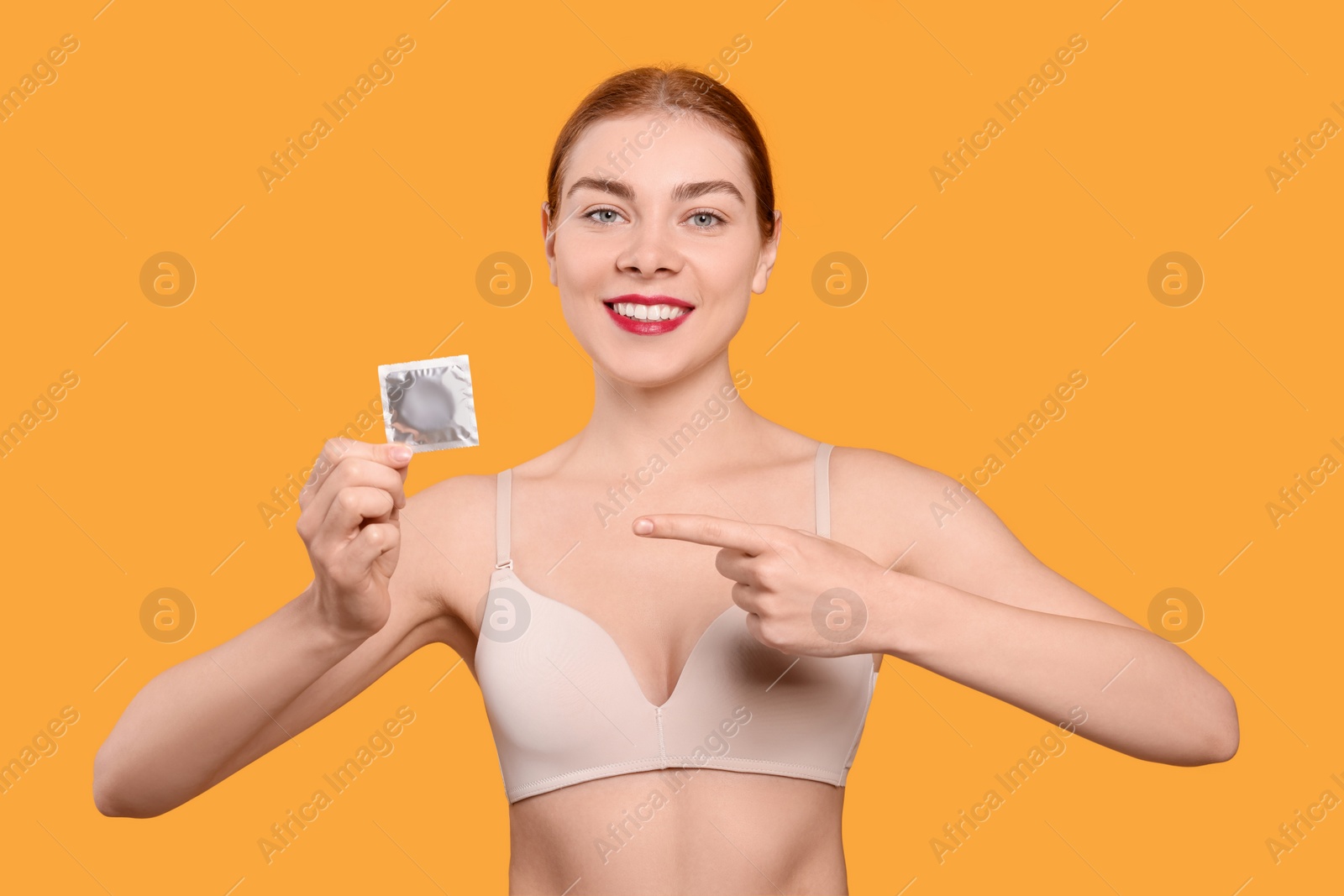 Photo of Woman in bra holding condom on yellow background. Safe sex