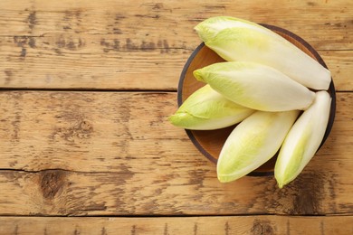 Photo of Fresh raw Belgian endives (chicory) in bowl on wooden table, top view. Space for text