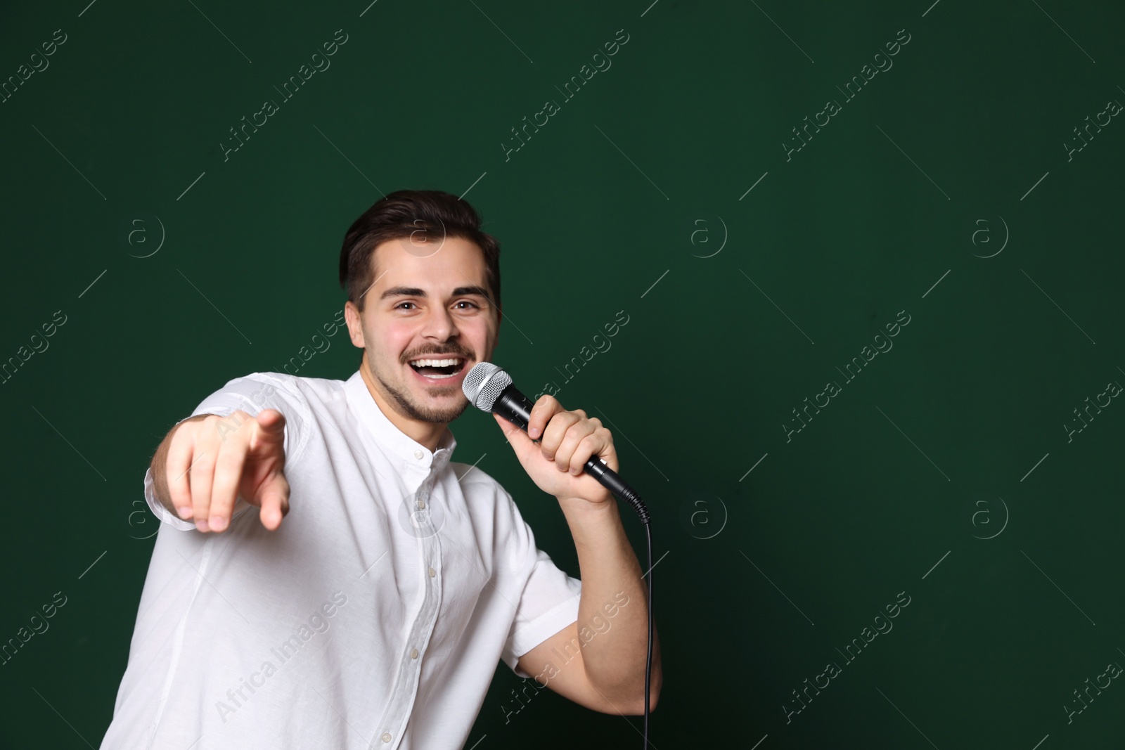 Photo of Young handsome man in casual clothes singing with microphone on color background. Space for text