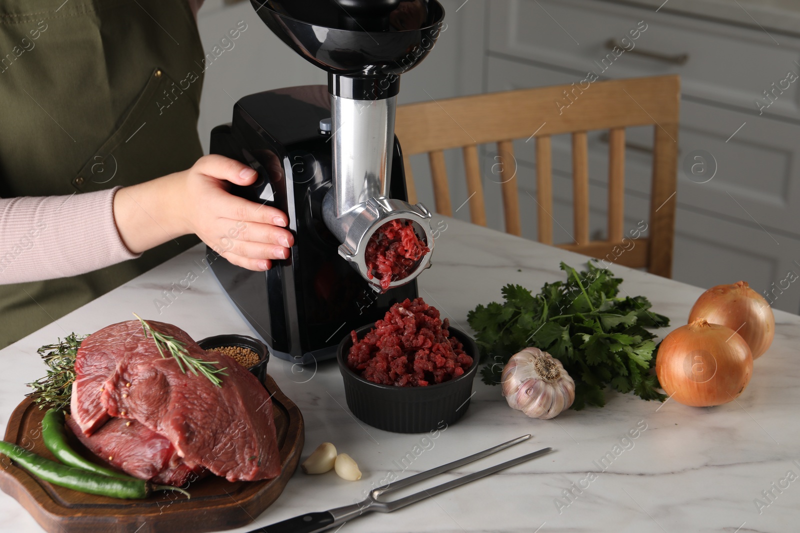 Photo of Woman making beef mince with electric meat grinder at white marble table in kitchen, closeup