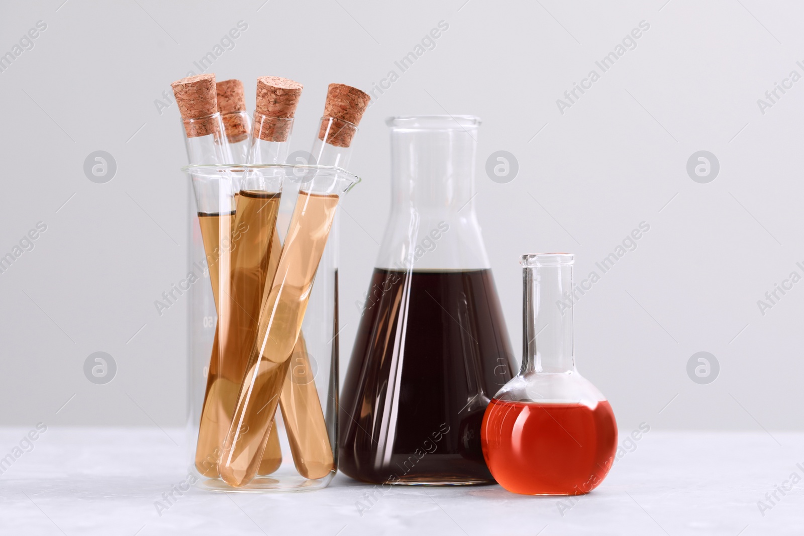 Photo of Different laboratory glassware with brown liquids on white table against light background