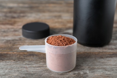 Photo of Scoop of chocolate protein powder on wooden table