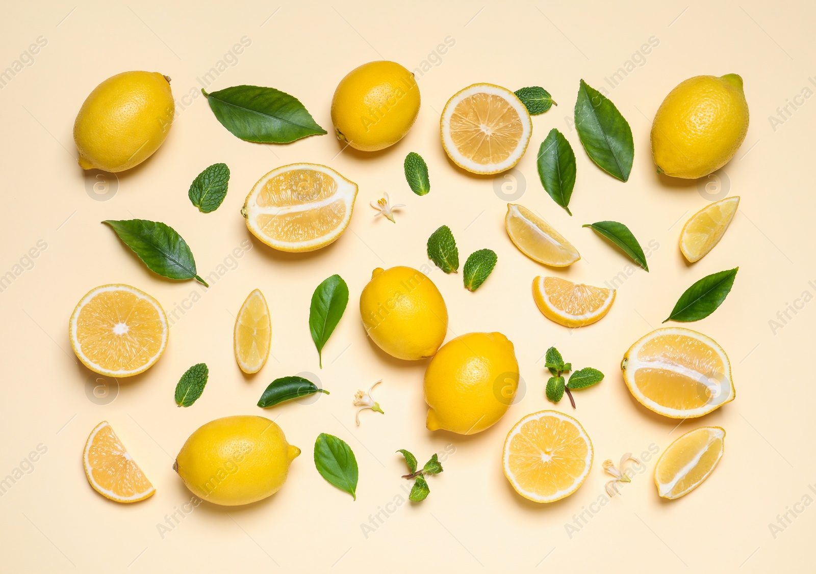 Photo of Many fresh ripe lemons with green leaves and flowers on beige background, flat lay