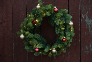 Photo of Beautiful Christmas wreath with baubles and string lights hanging on brown wooden wall