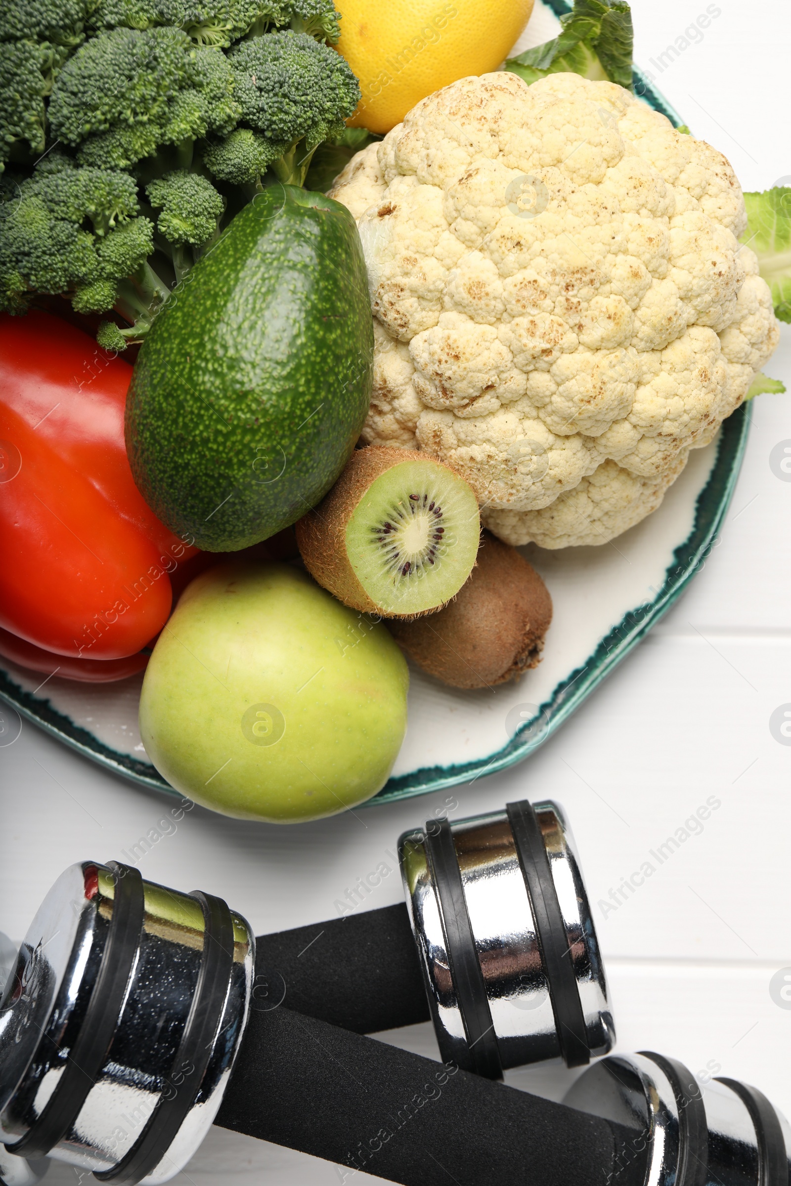 Photo of Healthy diet. Plate with products and dumbbells on white wooden table, flat lay