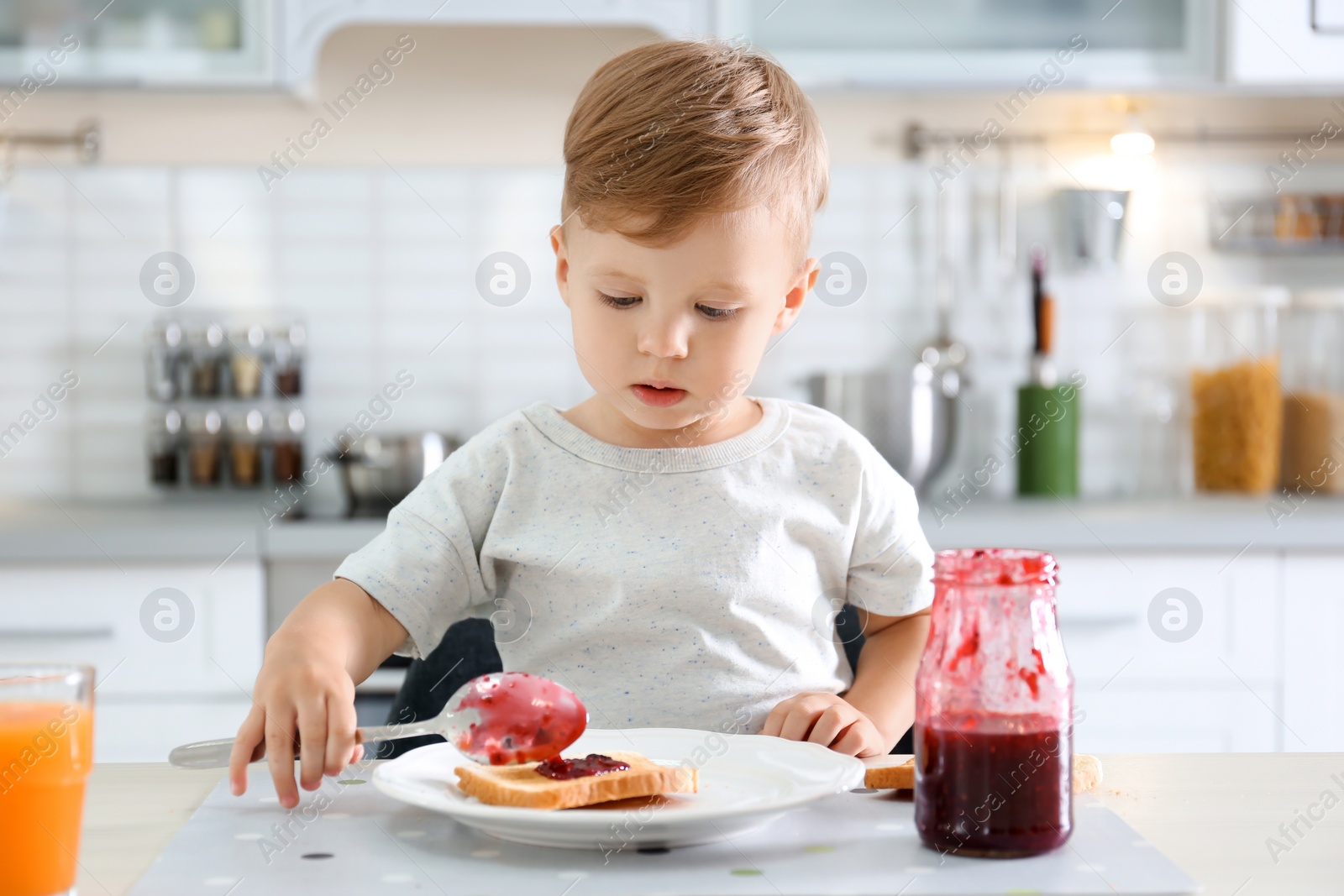 Photo of Little boy spreading jam on toast at table in kitchen