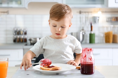 Little boy spreading jam on toast at table in kitchen