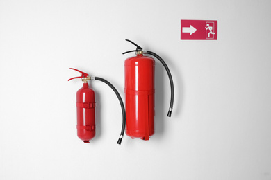 Photo of Different fire extinguishers and emergency exit sign on white wall