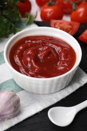 Organic ketchup in bowl, fresh tomatoes and garlic on black table, closeup. Tomato sauce