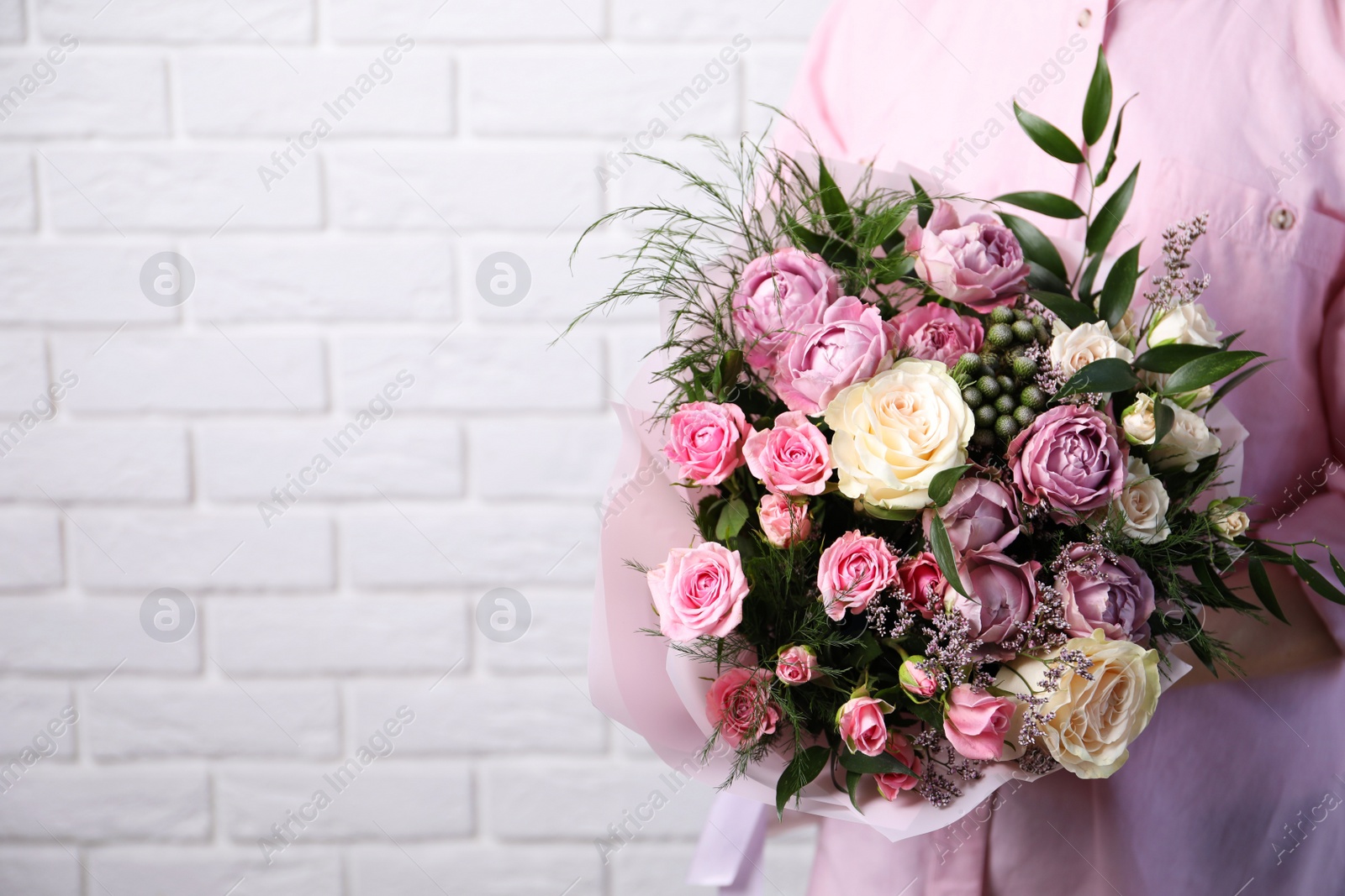 Photo of Woman with bouquet of beautiful roses near white brick wall, closeup. Space for text