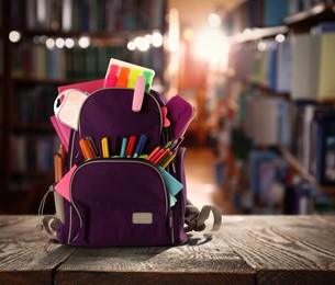 Backpack with school stationery on wooden table in library, space for text