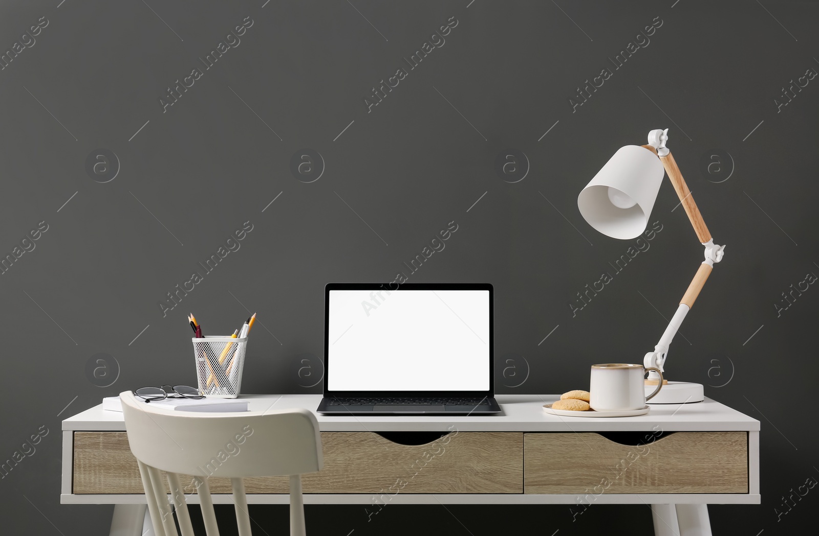 Photo of Stylish workplace with laptop, lamp and stationery on white table near grey wall