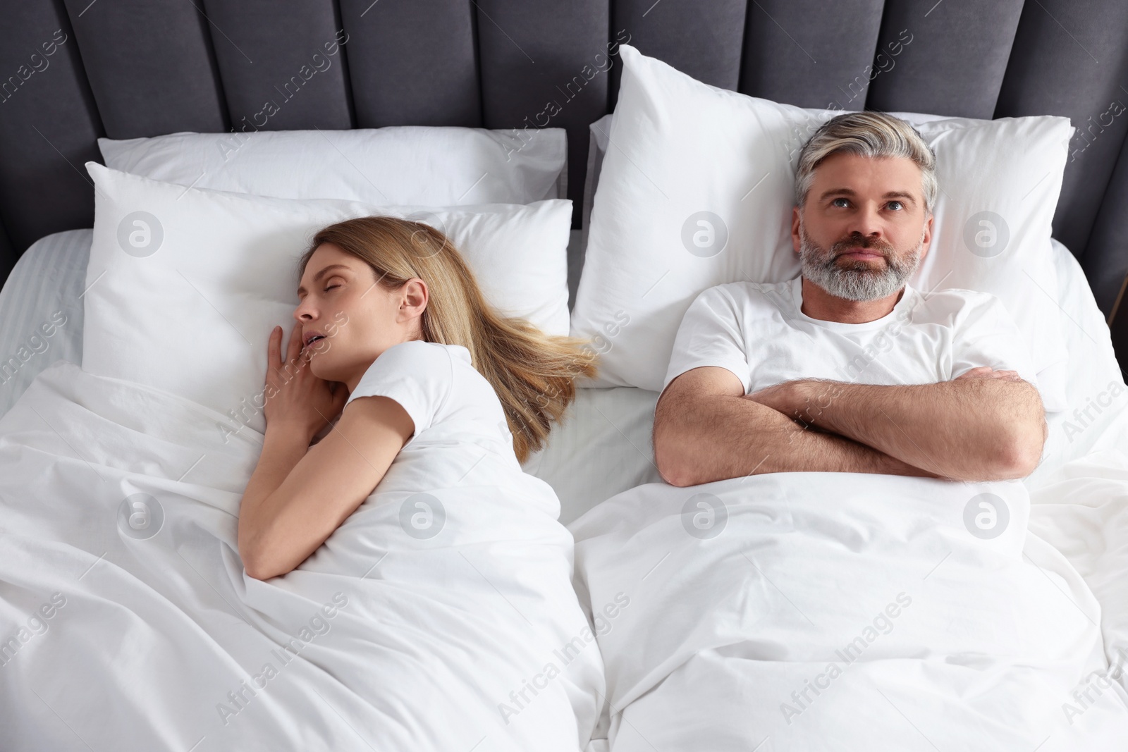 Photo of Irritated man lying near his snoring wife in bed at home