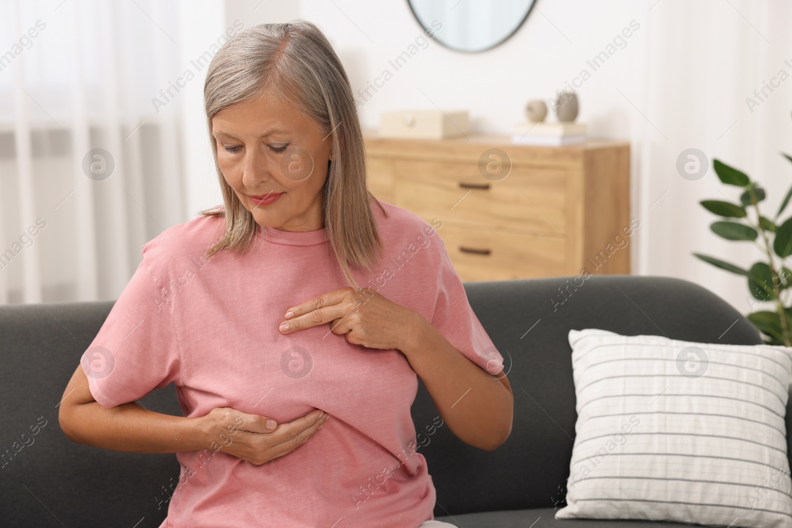 Photo of Beautiful senior woman doing breast self-examination at home, space for text