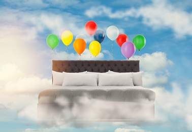 Image of Sweet dreams. Bed with bright air balloons in blue cloudy sky