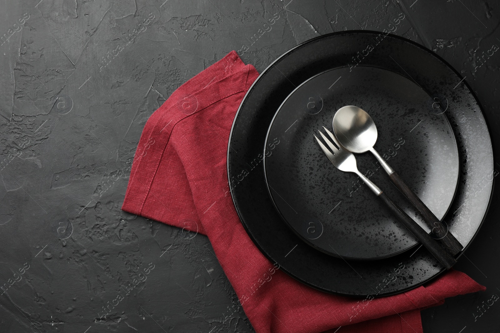 Photo of Stylish setting with cutlery, napkin and plates on dark textured table, top view. Space for text