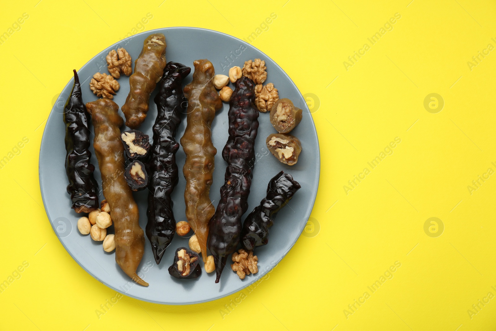 Photo of Plate with delicious churchkhelas and nuts on yellow background, top view. Space for text