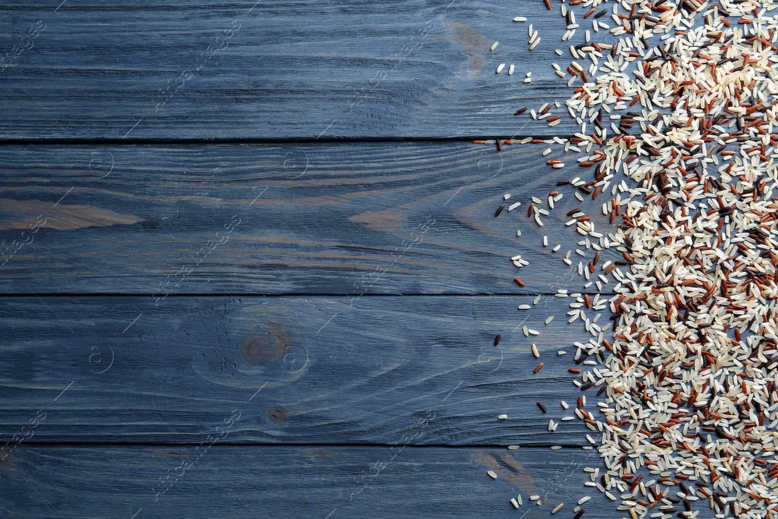 Photo of Brown and other types of rice scattered on color wooden background. Space for text