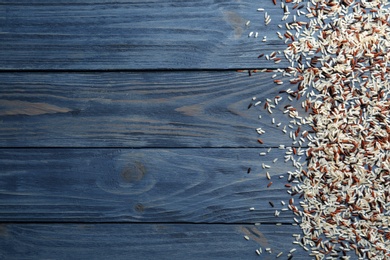 Photo of Brown and other types of rice scattered on color wooden background. Space for text