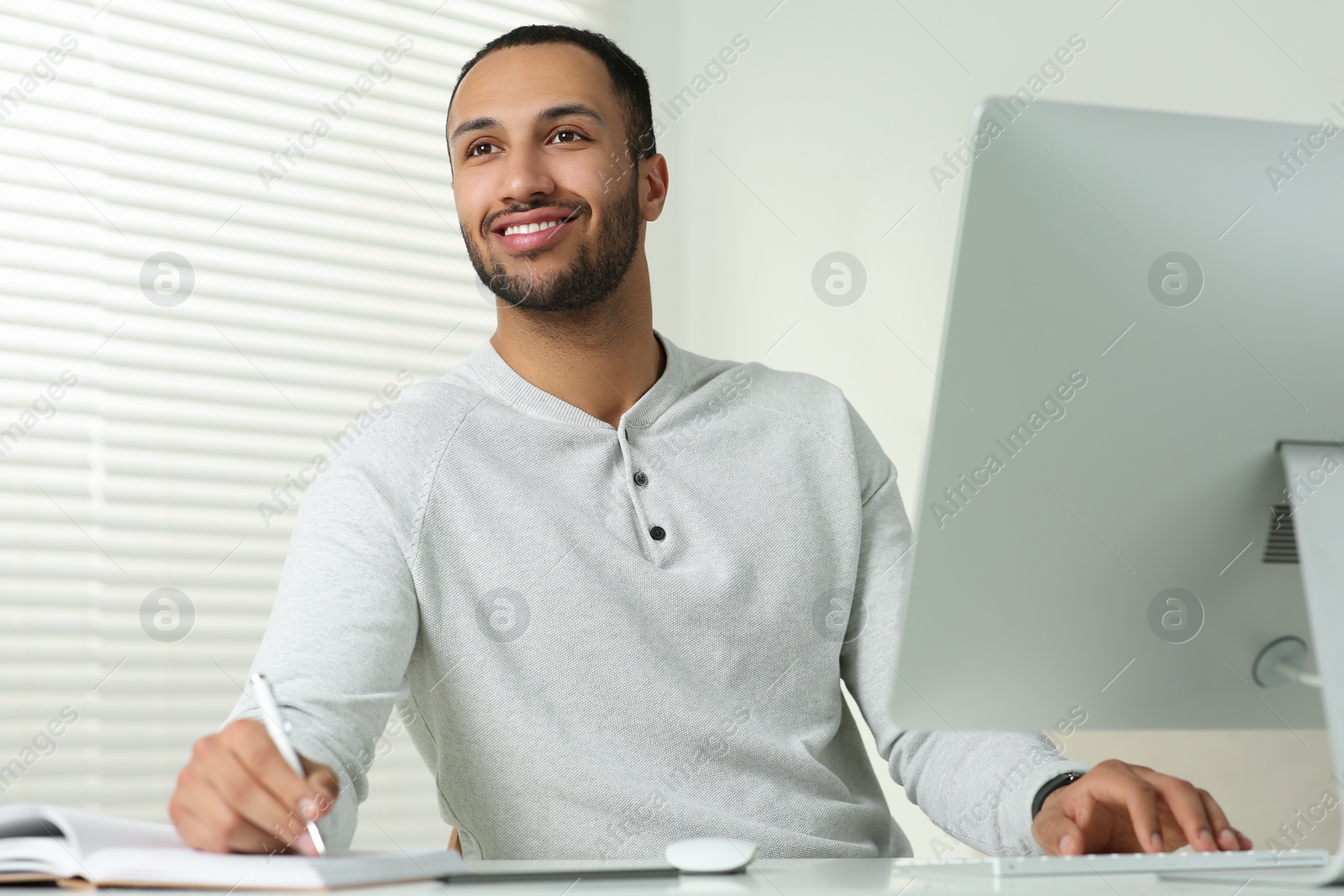 Photo of Young man working on computer at desk in room. Home office