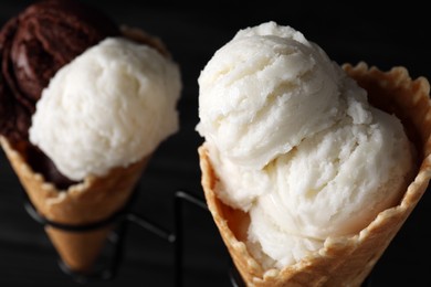 Photo of Ice cream scoops in wafer cones on stand against dark background, closeup