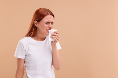 Suffering from allergy. Young woman with tissue sneezing on beige background, space for text