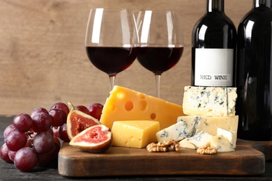Photo of Different delicious cheeses, fruits and wine on table against wooden background