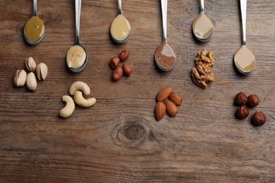 Photo of Jars with butters made of different nuts and ingredients on wooden table, flat lay. Space for text