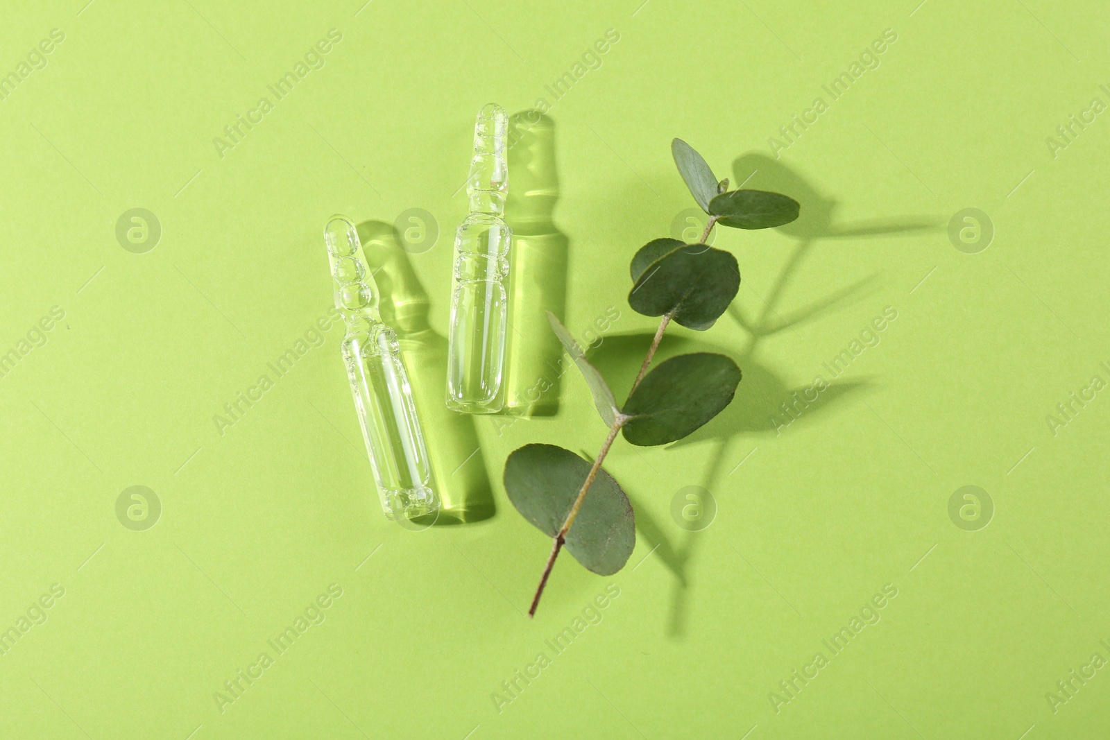 Photo of Glass ampoules with liquid and leaves on light green background, top view