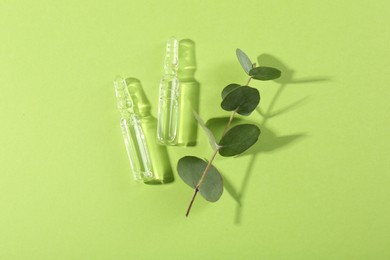 Glass ampoules with liquid and leaves on light green background, top view