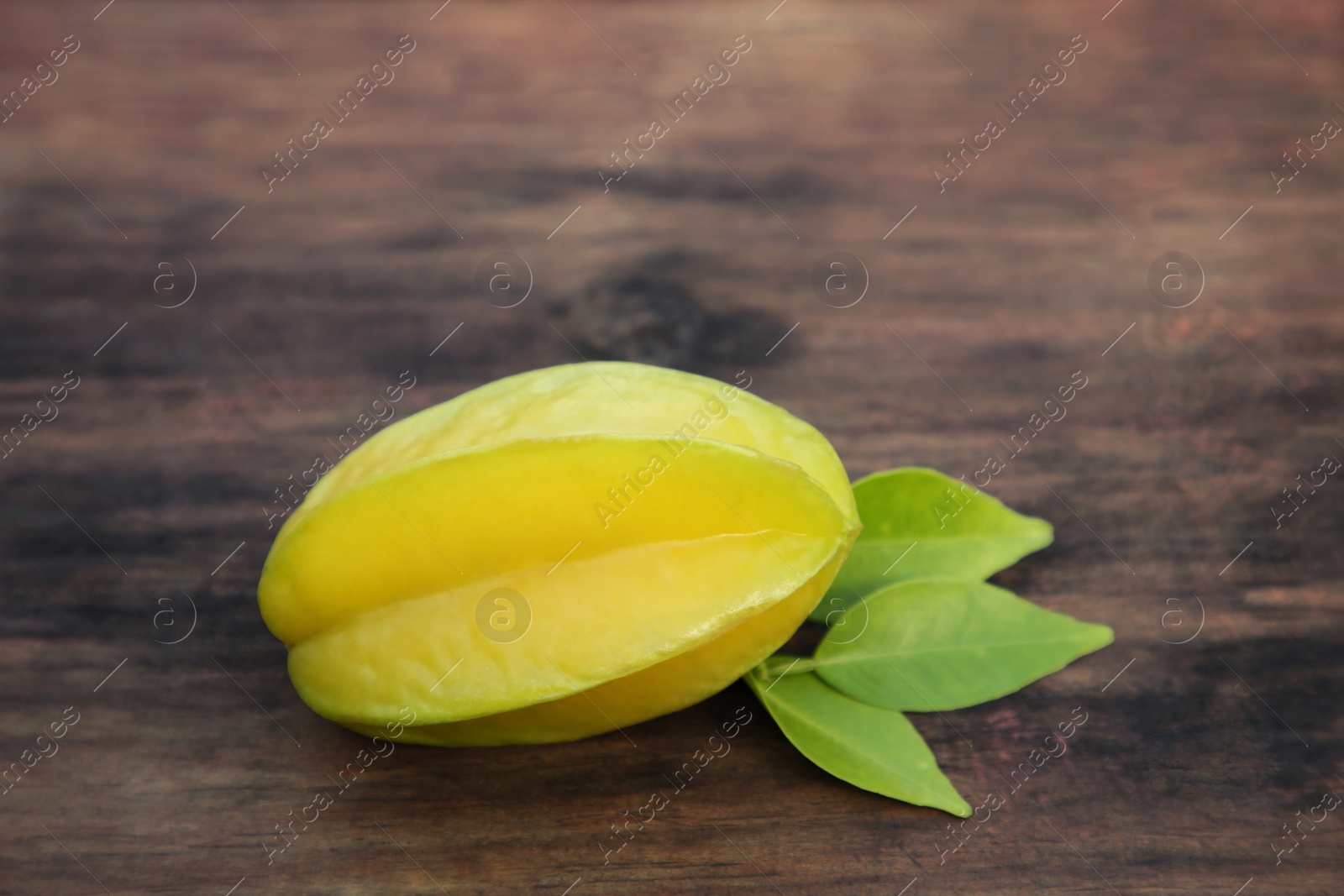 Photo of Delicious ripe carambola with leaves on wooden table