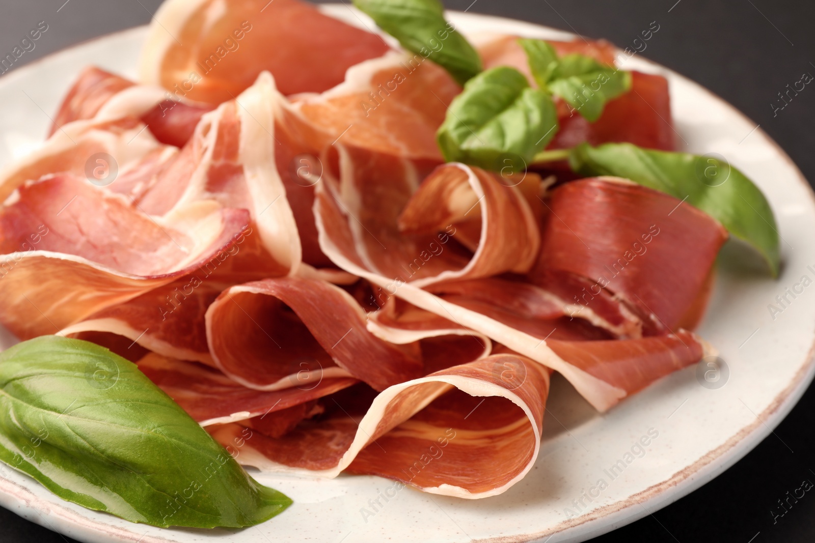 Photo of Slices of tasty cured ham and basil on plate, closeup