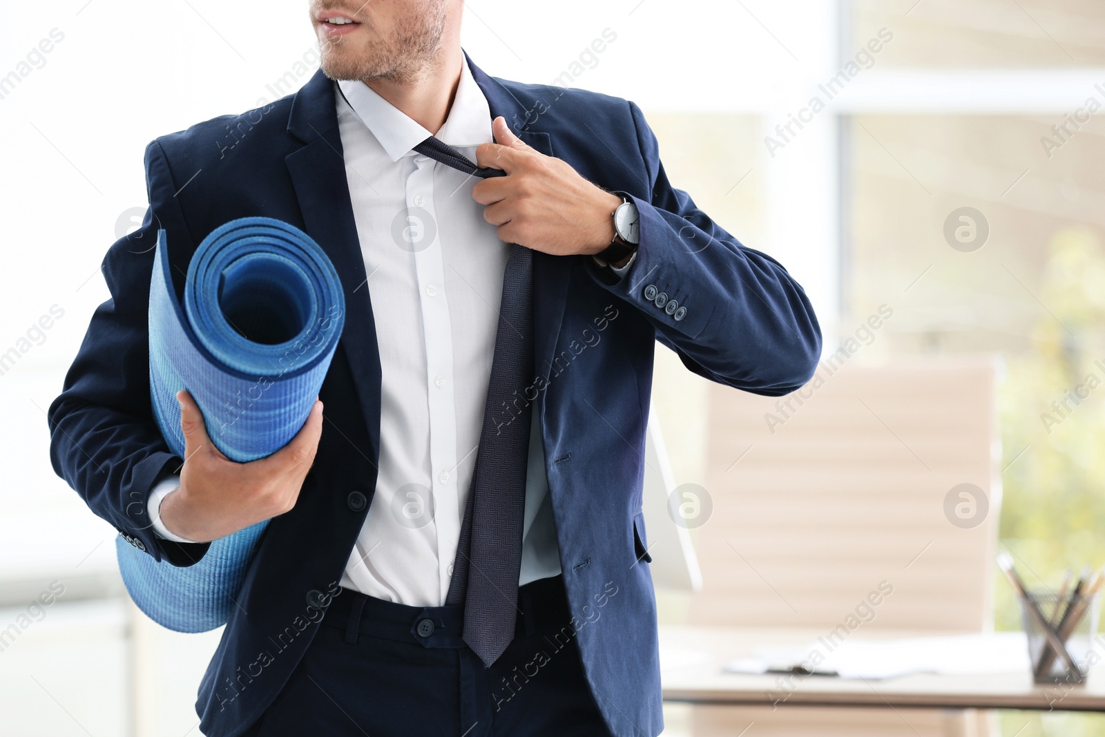 Photo of Young handsome businessman holding yoga mat in office. Gym after work