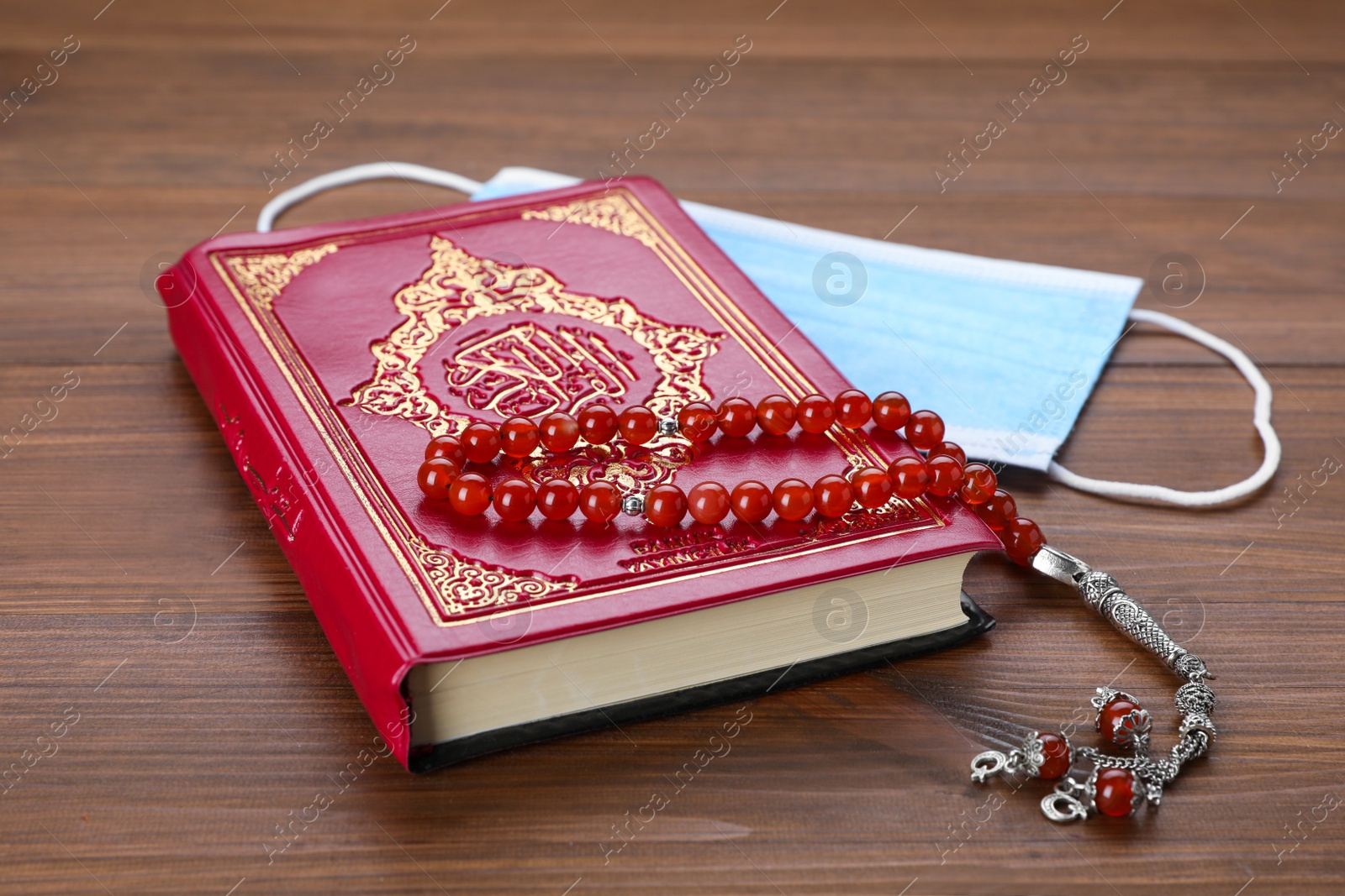Photo of Muslim prayer beads, Quran and protective mask on wooden table