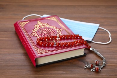 Muslim prayer beads, Quran and protective mask on wooden table