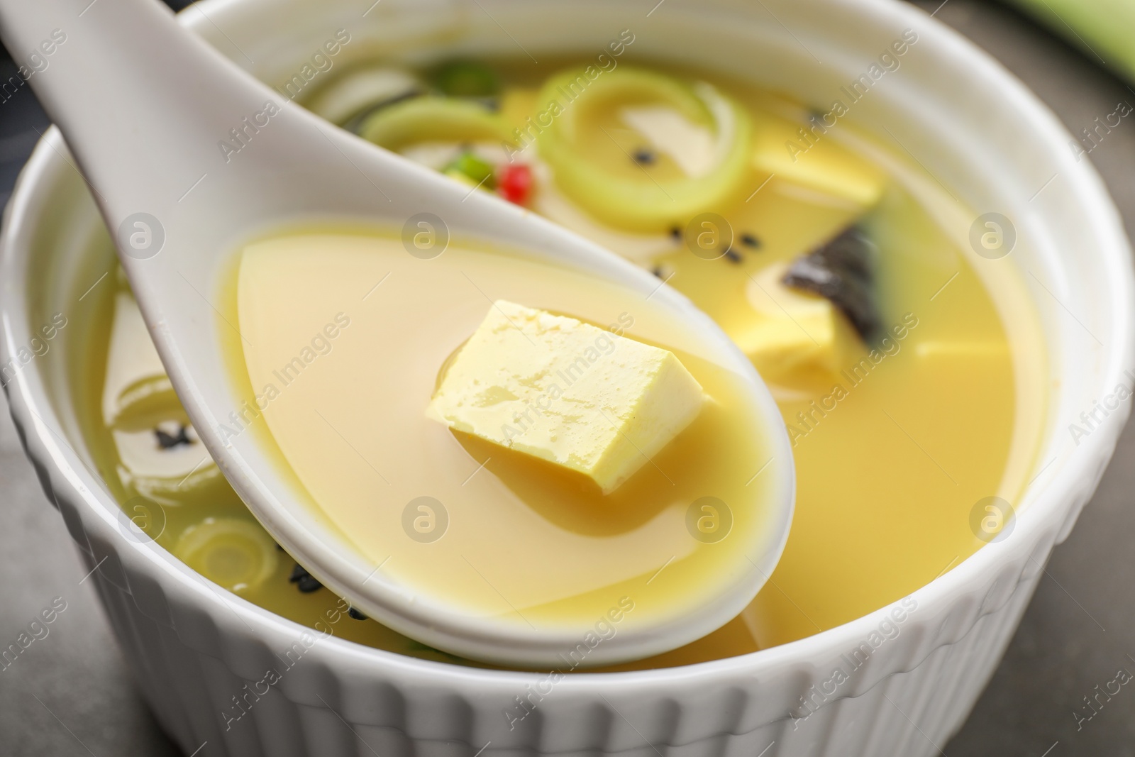 Photo of Eating delicious miso soup with tofu from bowl on table, closeup