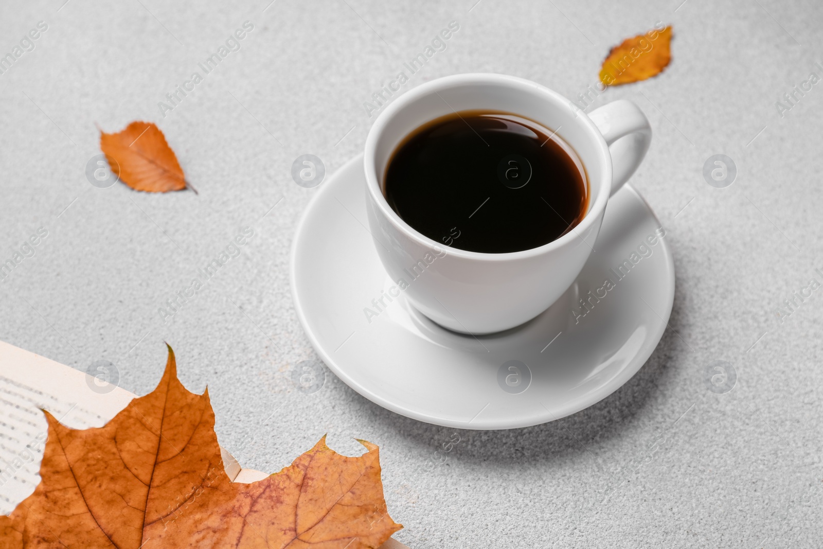 Photo of Cup of hot drink, book and autumn leaves on light grey textured table