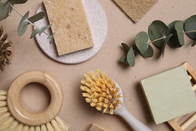 Photo of Cleaning brushes, soap bars and eucalyptus leaves on pale brown background, flat lay