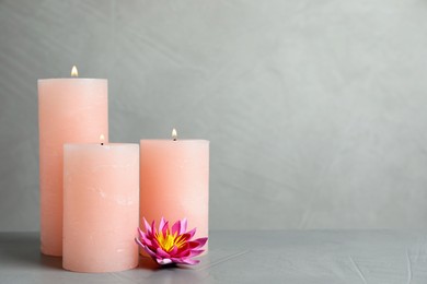 Photo of Burning candles and lotus flower on light grey stone table. Space for text