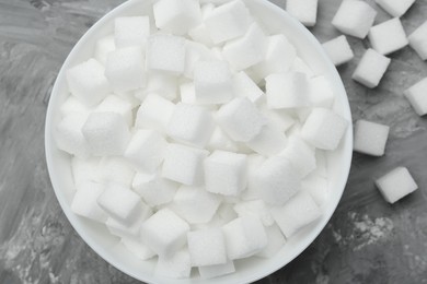 Photo of White sugar cubes in bowl on grey table, top view