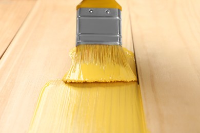 Applying yellow paint onto wooden surface, closeup