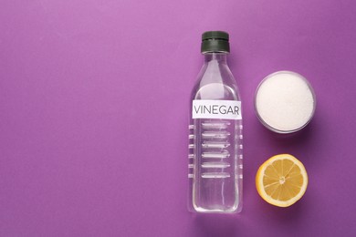 Photo of Eco friendly natural cleaners. Vinegar in bottle, cut lemon and bowl of soda on purple background, flat lay. Space for text